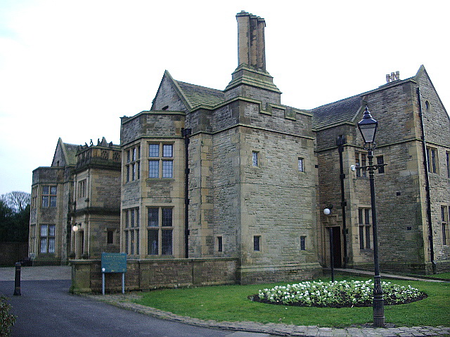 The Haworth Art Gallery in Accrington: a substantial early twentieth-century stone house with mullioned windows, gables and tall chimneys, a lamp post in front and a circular flower bed of white flowers on the lawn