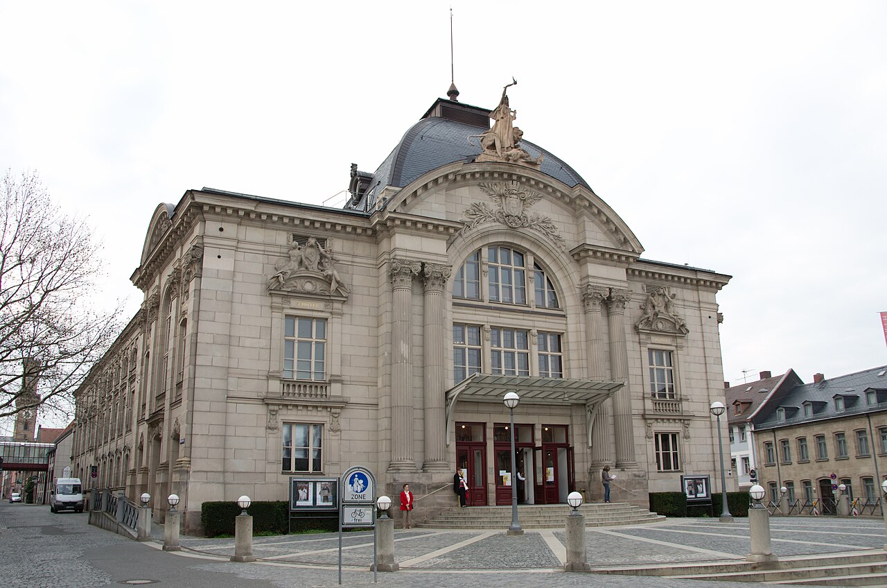 The Stadttheater in Fürth: an ornate pale stone theatre with a domed roof, a large arched window over the entrance, Corinthian columns and sculpted figures on the roofline and pediments, standing on an open paved square