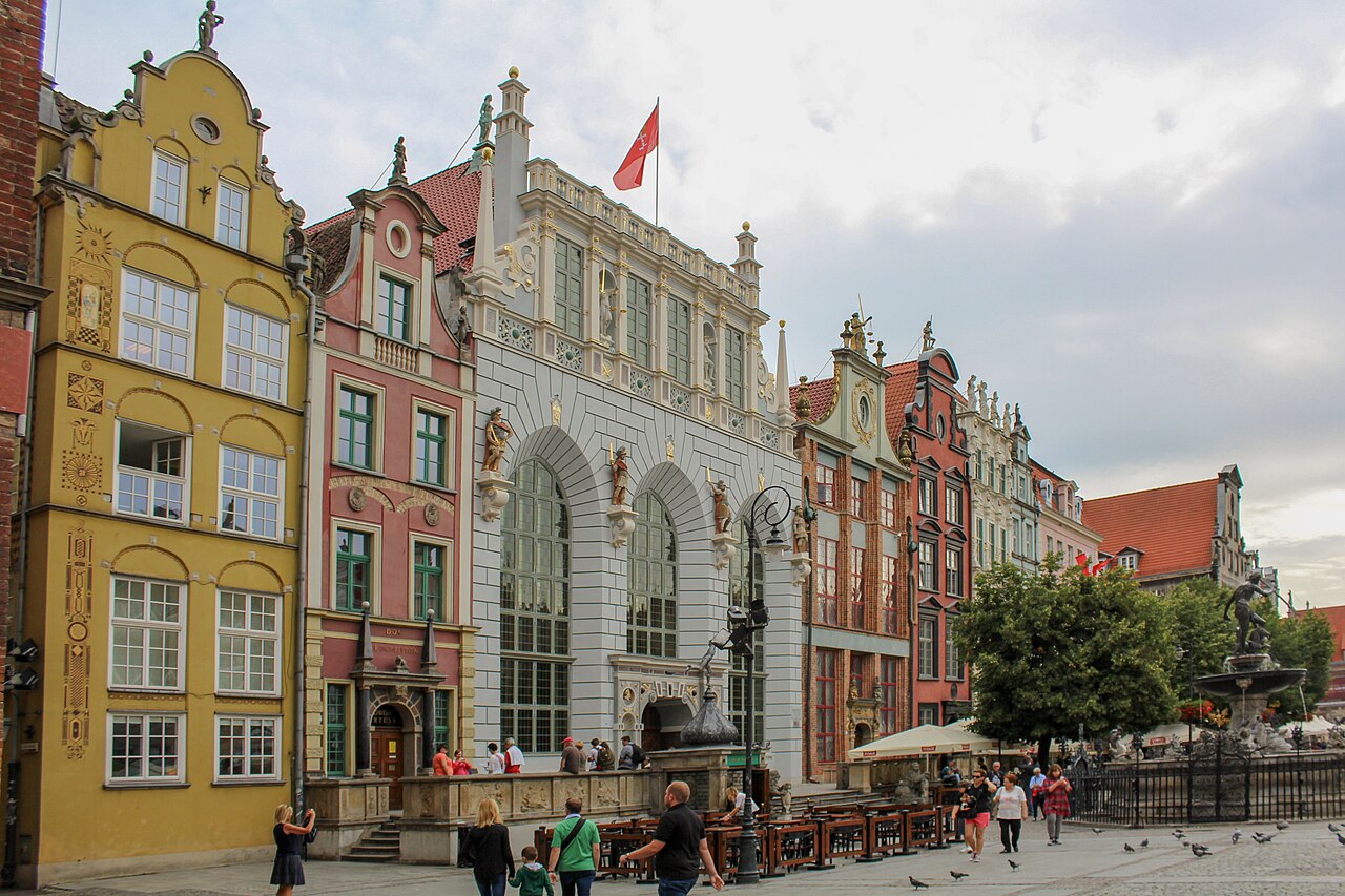 Długi Targ in Gdańsk: a row of tall gabled merchant houses in yellow, pink, grey and red with sculpted facades, the arcaded Artus Court in the centre and the Neptune fountain behind railings on the right
