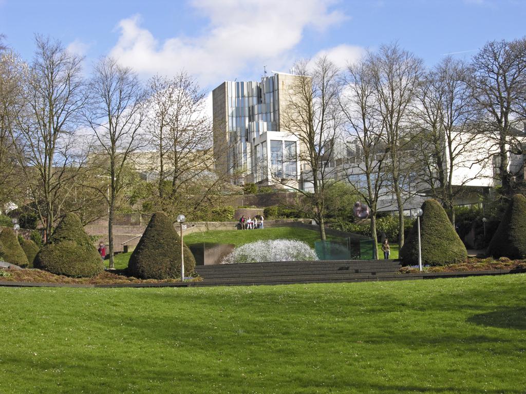 Museum Abteiberg in Mönchengladbach seen across a lawn in its sculpture garden: an angular building of white panels and glass stepping down a hillside, with clipped conical hedges and bare trees in front
