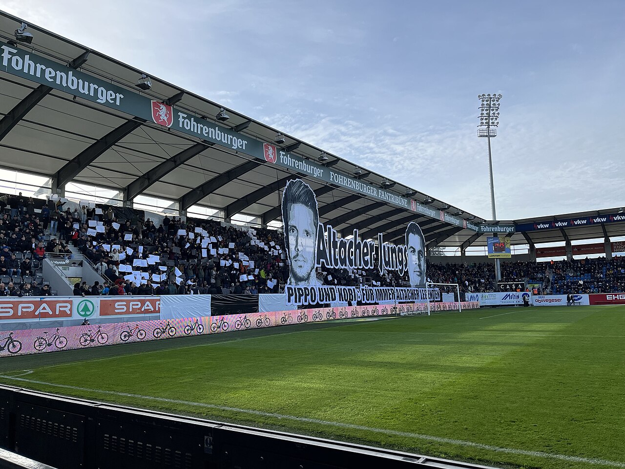 A home stand filling up before kick-off, with supporters holding up cards to form a tifo across the terrace
