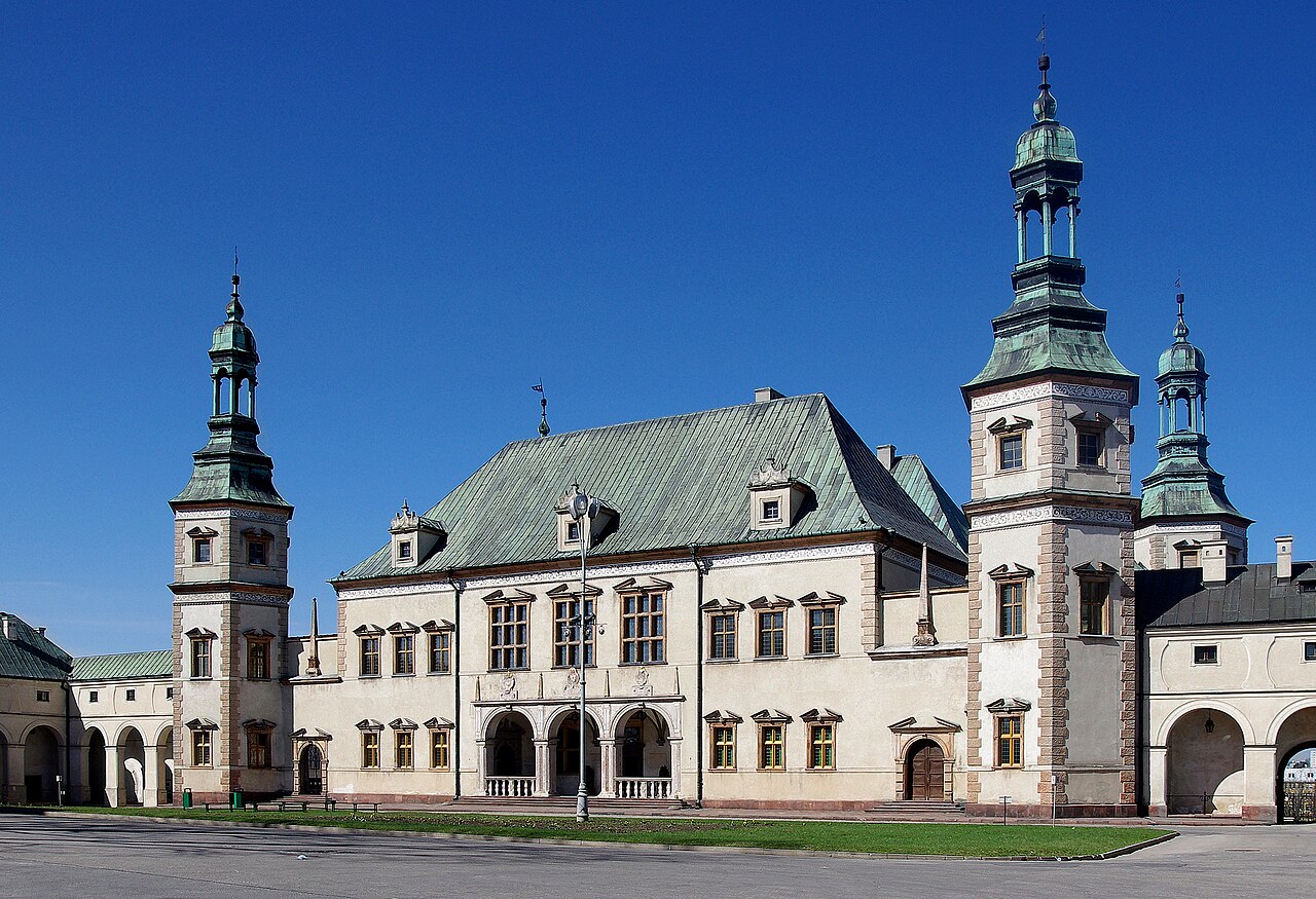 The Palace of the Kraków Bishops in Kielce: a long white seventeenth-century residence with a green copper roof, flanked by four towers with green onion-domed tops, under a deep blue sky