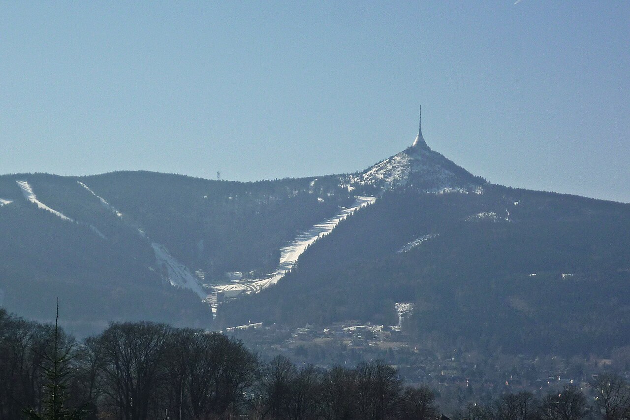 Ještěd mountain above Liberec in winter, a forested ridge with white ski runs cut into it and the pointed silhouette of the hotel and transmitter tower on the summit