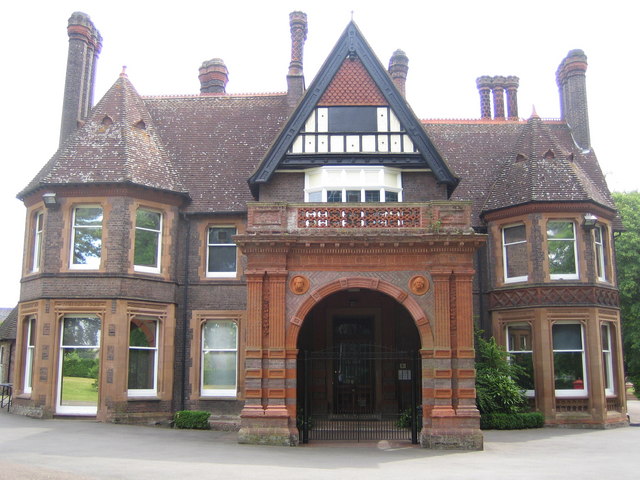 Wardown House in Luton: an ornate red-brick Victorian mansion with tall decorated chimneys, bay windows, a black and white timbered gable and a deep terracotta porch over an arched entrance