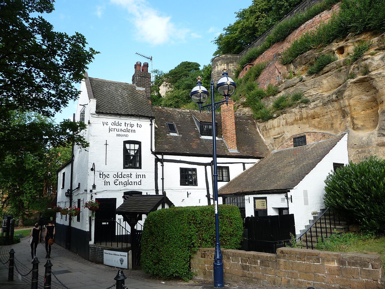Ye Olde Trip to Jerusalem in Nottingham: a whitewashed pub with tiled roofs built directly against a tall sandstone cliff, with the words ye olde trip to jerusalem 1189 AD and the oldest inn in England painted on its gable end