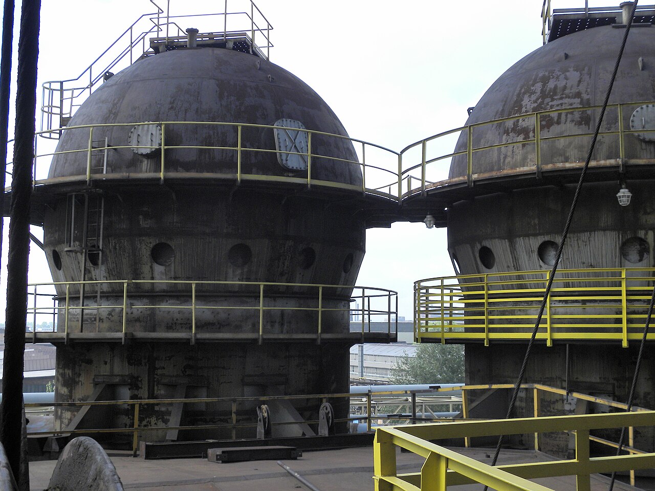 Two enormous rusted steel spheres at Dolní Vítkovice in Ostrava, ringed with yellow steel walkways and connected by a bridge, part of the preserved ironworks complex