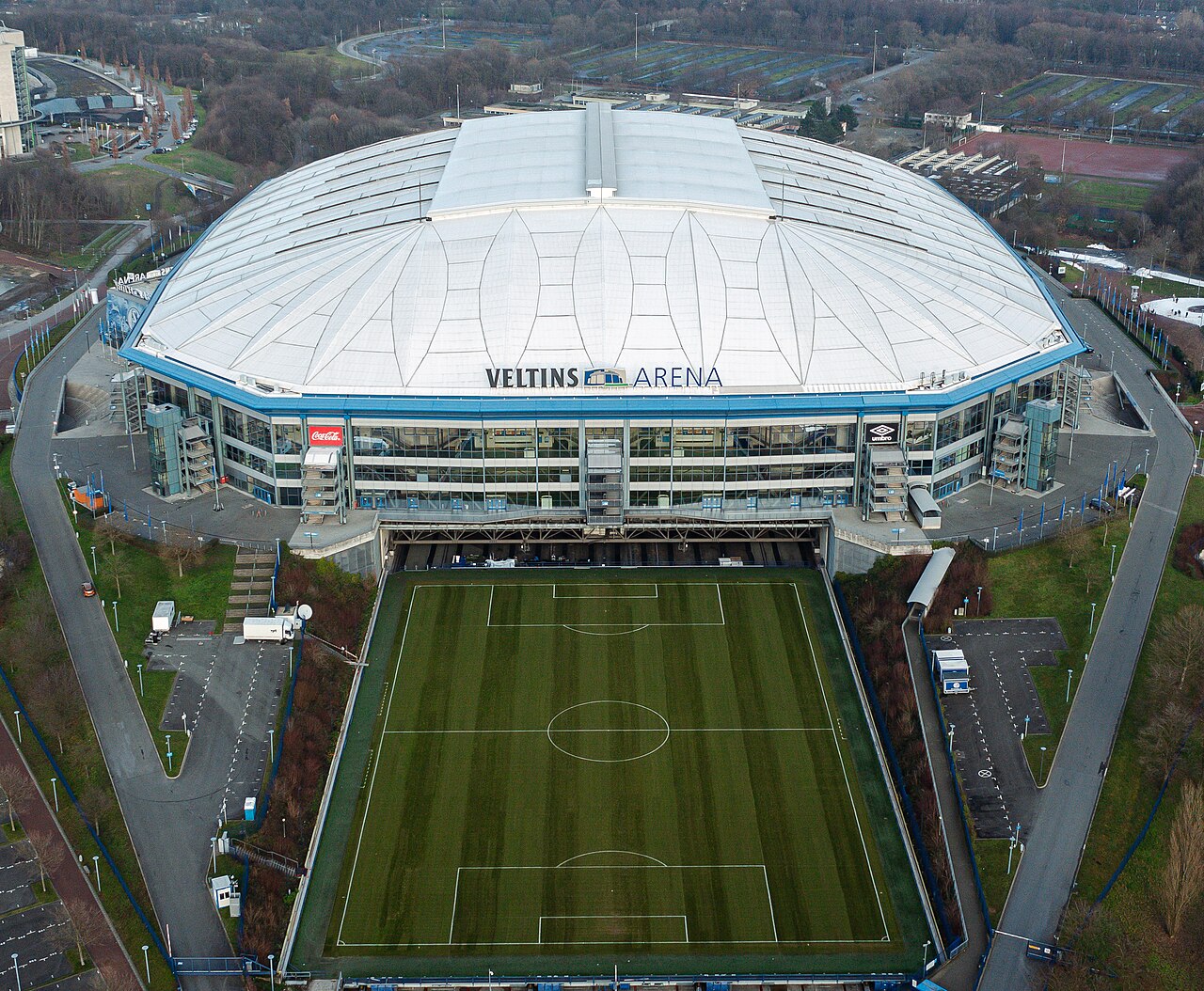 The Veltins-Arena from the air with its roof closed and the entire playing surface slid out of the building, the pitch sitting on an apron in front of the stadium