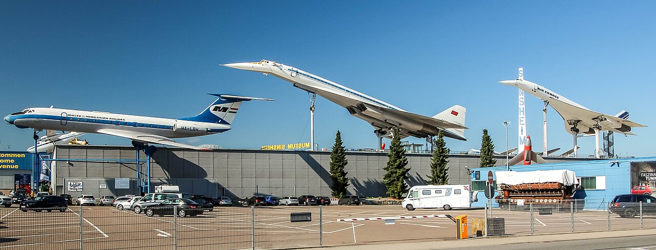 The roof of the Technik Museum Sinsheim: an Air France Concorde and a Soviet Tupolev Tu-144 mounted nose-up as if climbing, with a Malev Tu-134 alongside them, above the museum hall and its car park