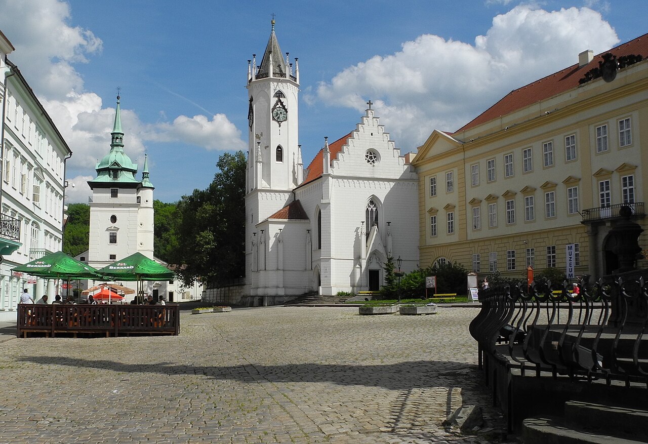 Zámecké náměstí in Teplice: a cobbled square with a white Gothic church, a baroque bell tower with a green copper dome, a yellow chateau housing the museum, and a beer garden with green parasols to one side