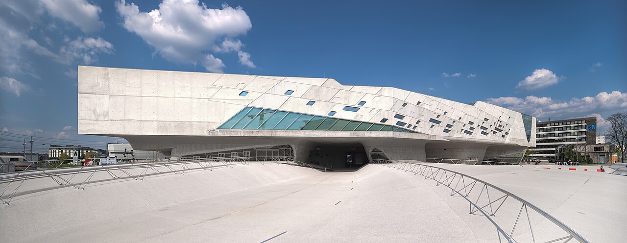 The Phaeno science centre in Wolfsburg: a large angular pale concrete building with irregular windows, raised off the ground on curved conical legs, standing above an open sculpted concrete plaza